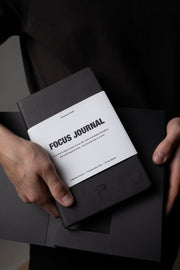 Black 'Focus Journal' held by a person against a dark background